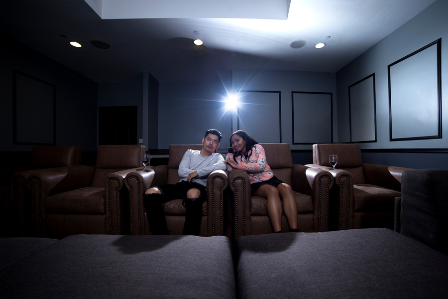 Two people sitting in plush chairs in a home theater room, facing the screen that’s off-camer