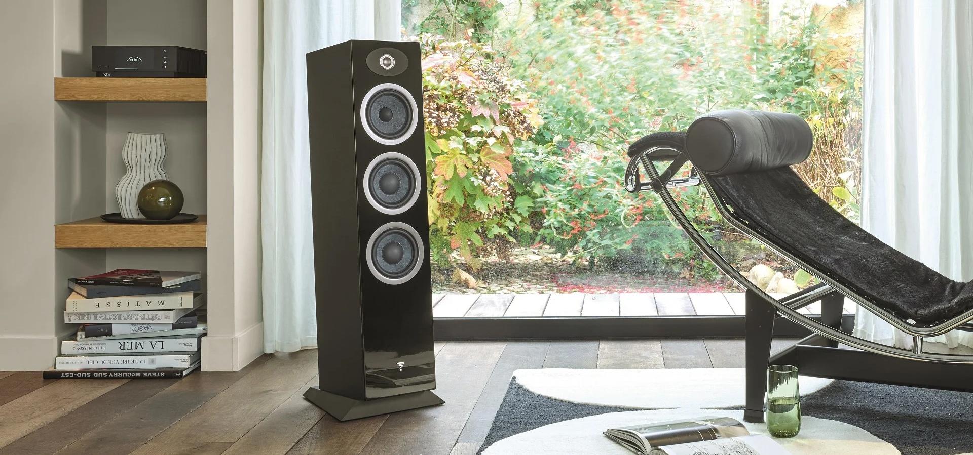 Sleek black floorstanding speaker next to lounge chair in modern room with garden view