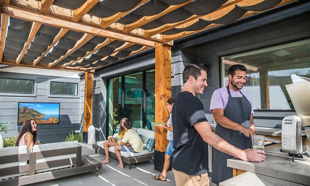 <span class="uk-h4">friends gather in an outdoor seating and grilling area. A wall-mounted Sunbrite TV shows an ultra-bright nature scene.</span>