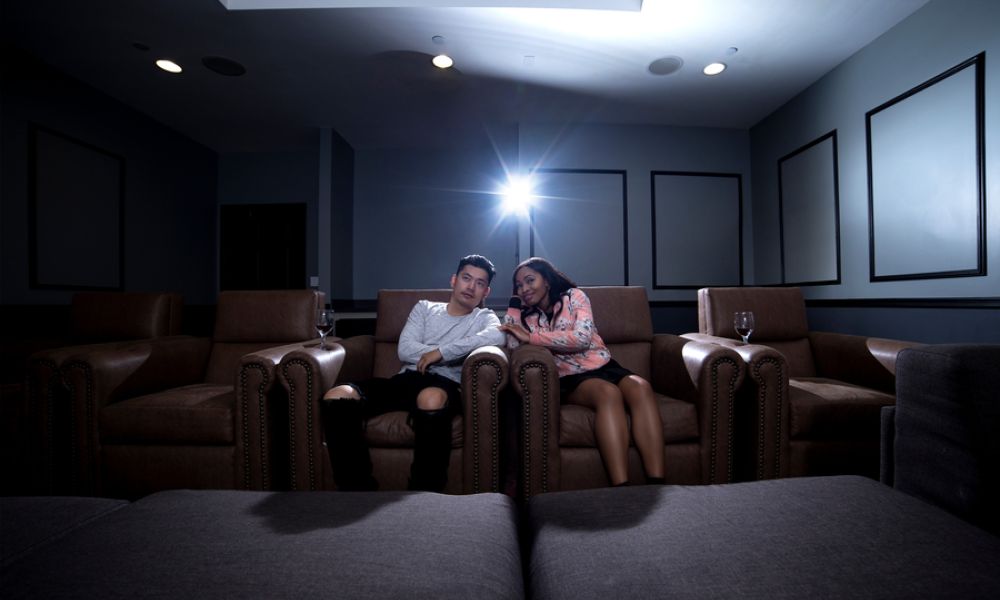 <span class="uk-h4">Two people sitting in plush chairs in a home theater room, facing the screen that’s off-camer</span>
