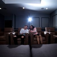 Two people sitting in plush chairs in a home theater room, facing the screen that’s off-camer