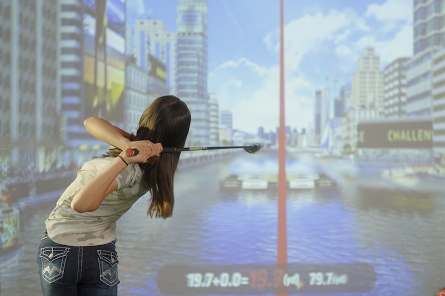 A golfer using a home golf simulator takes a virtual swing down the Chicago riverfront.